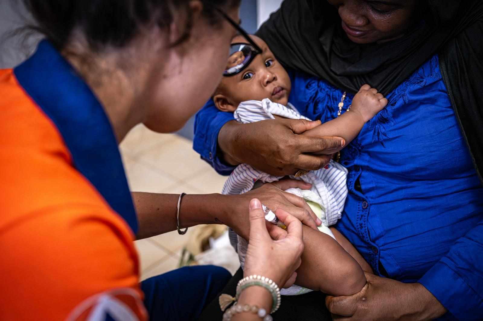 Une soignante de la Protection Civile Santé Mayotte vaccine un nourrisson que sa mère tient dans ses bras.